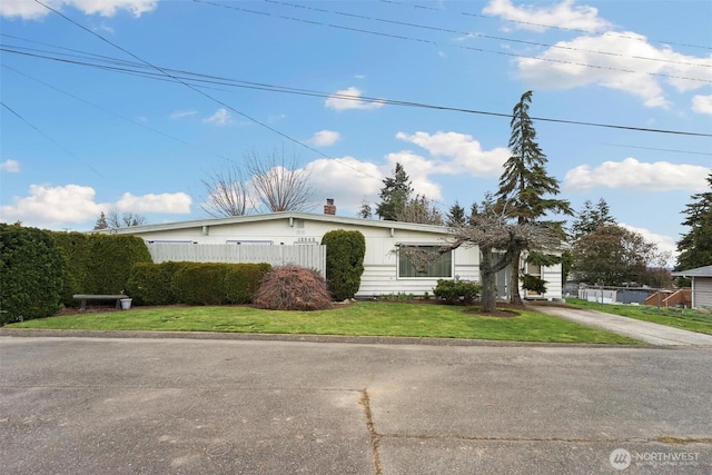 view of front facade featuring a front lawn, concrete driveway, and fence