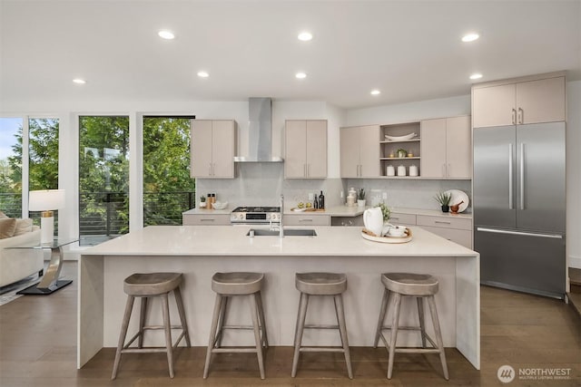 kitchen with backsplash, wall chimney range hood, light countertops, appliances with stainless steel finishes, and a sink