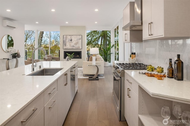 kitchen featuring a fireplace, stainless steel appliances, a sink, an AC wall unit, and wall chimney range hood