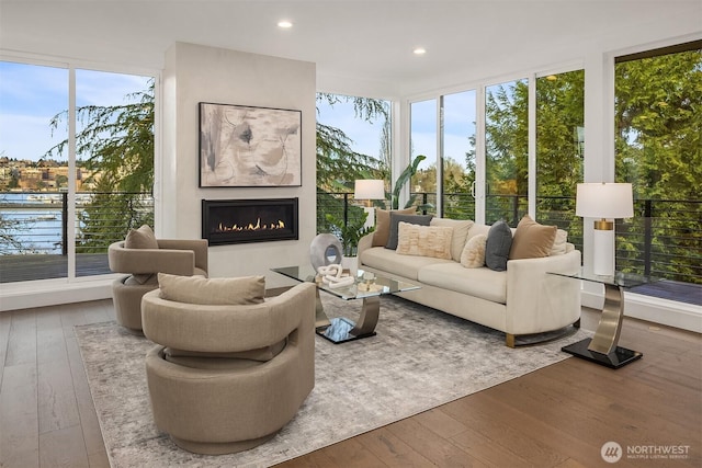 living room with a glass covered fireplace, a wall of windows, recessed lighting, and wood-type flooring