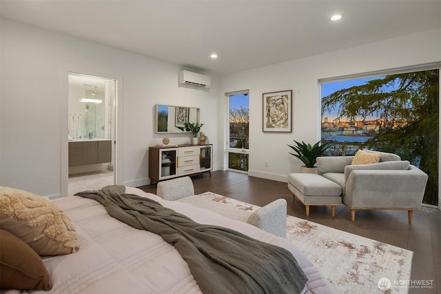 bedroom with wood finished floors, a wall unit AC, recessed lighting, connected bathroom, and baseboards