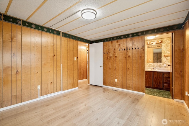 spare room with baseboards, wooden walls, and wood finished floors