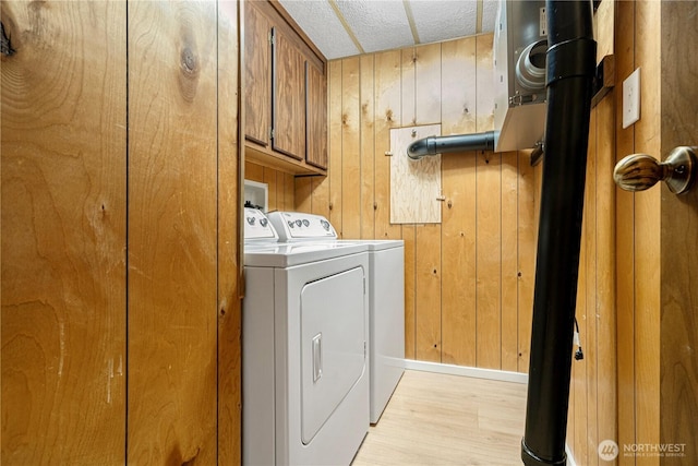 laundry room with baseboards, wood walls, light wood-style flooring, cabinet space, and independent washer and dryer