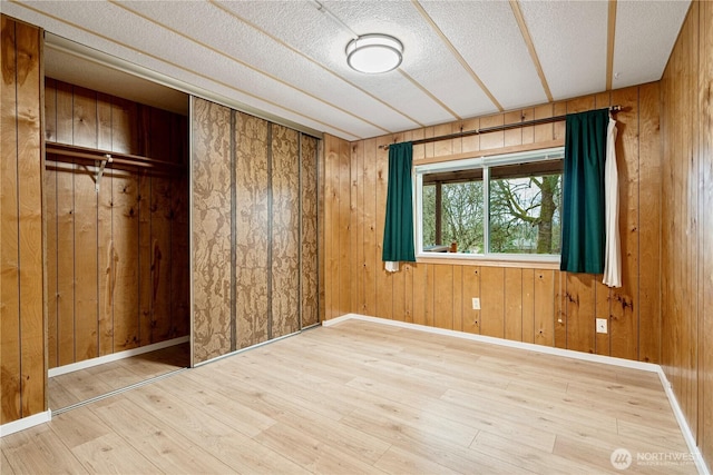 unfurnished bedroom featuring wood finished floors, baseboards, wood walls, and a textured ceiling