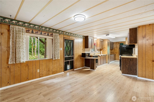 kitchen with light wood-type flooring, brown cabinets, stainless steel microwave, light countertops, and baseboards