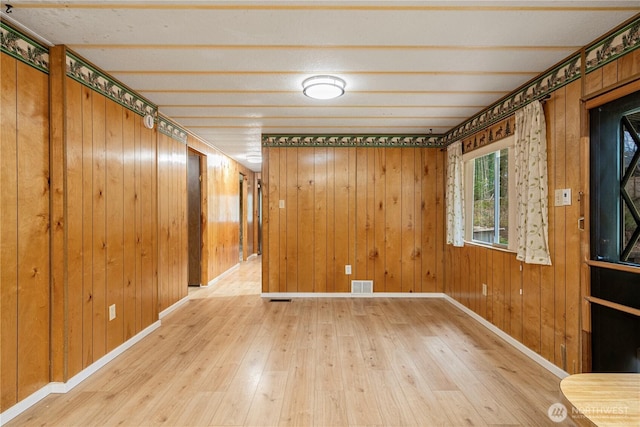 spare room featuring visible vents, wood walls, baseboards, and wood finished floors