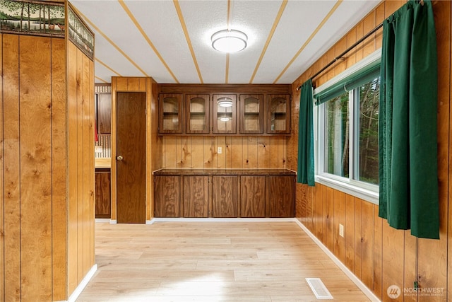 spare room with visible vents, a textured ceiling, wood walls, light wood finished floors, and baseboards