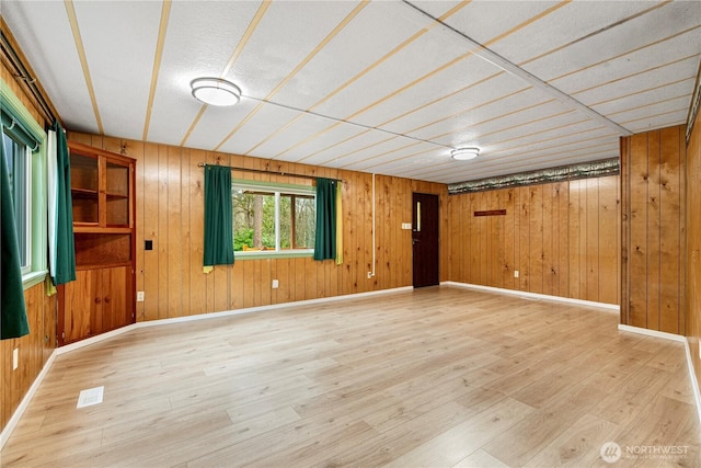 interior space with light wood finished floors, visible vents, wood walls, and baseboards