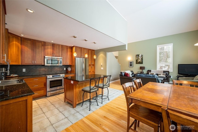 kitchen featuring a breakfast bar, a sink, tasteful backsplash, open floor plan, and appliances with stainless steel finishes