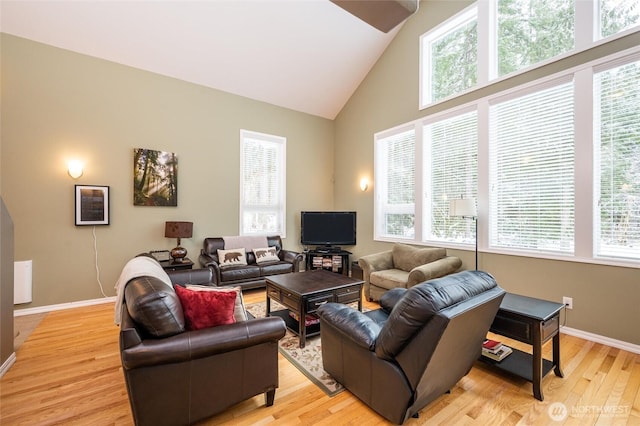 living area with light wood-style flooring, high vaulted ceiling, and baseboards