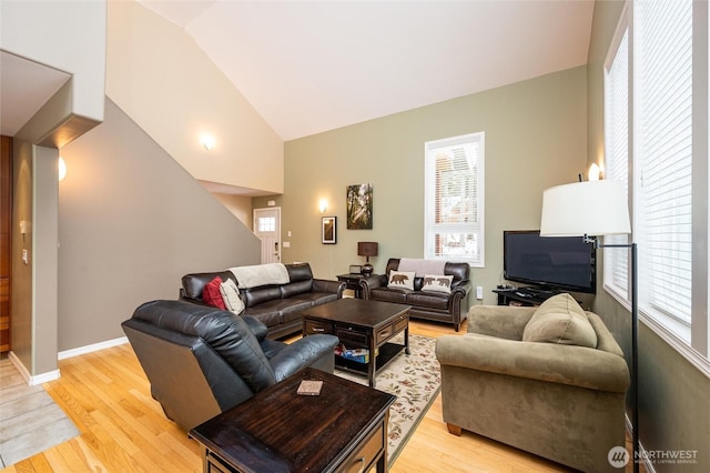 living area with baseboards, lofted ceiling, plenty of natural light, and light wood-style flooring