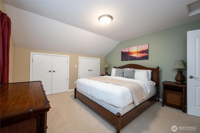 bedroom with light colored carpet, two closets, baseboards, and vaulted ceiling