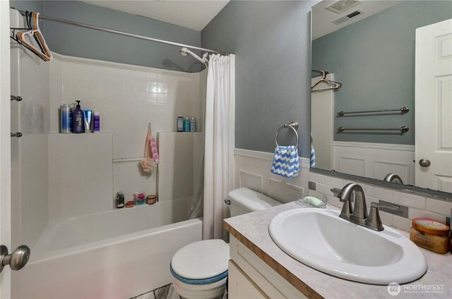 bathroom with vanity, shower / bathtub combination with curtain, visible vents, a wainscoted wall, and toilet