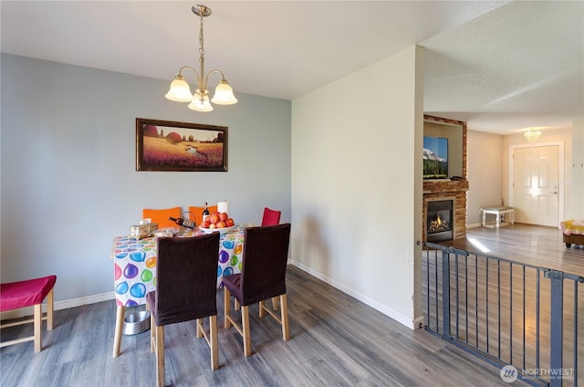 dining space featuring baseboards, a large fireplace, wood finished floors, and a chandelier