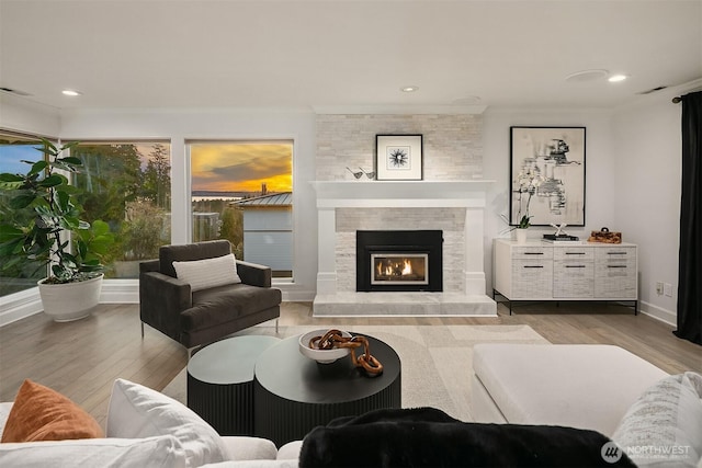 living area with a stone fireplace, crown molding, wood finished floors, and visible vents