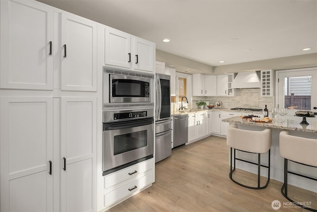 kitchen featuring appliances with stainless steel finishes, light stone countertops, custom range hood, and a sink