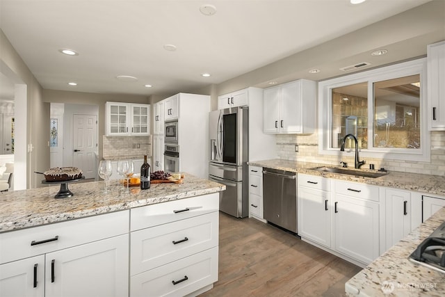 kitchen featuring a sink, wood finished floors, stainless steel appliances, white cabinets, and light stone countertops