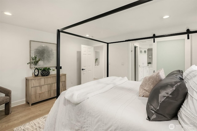 bedroom with recessed lighting, connected bathroom, light wood-style floors, and a barn door