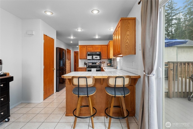 kitchen featuring tile counters, a peninsula, light tile patterned flooring, stainless steel appliances, and a sink