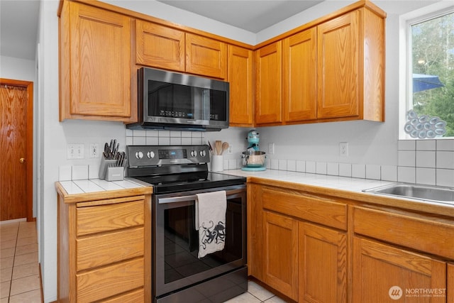 kitchen featuring tile counters, light tile patterned floors, brown cabinets, and stainless steel appliances