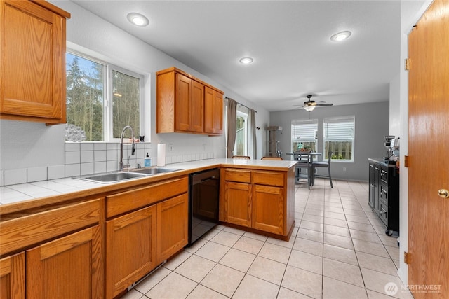 kitchen featuring tile countertops, black dishwasher, light tile patterned floors, a peninsula, and a sink