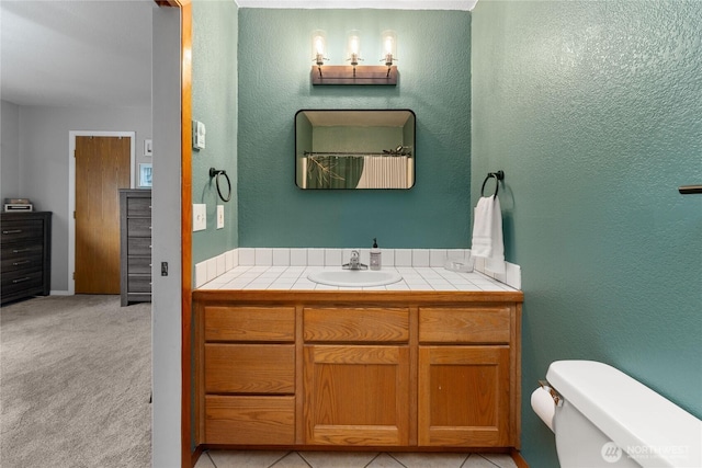 full bathroom with vanity, toilet, and a textured wall