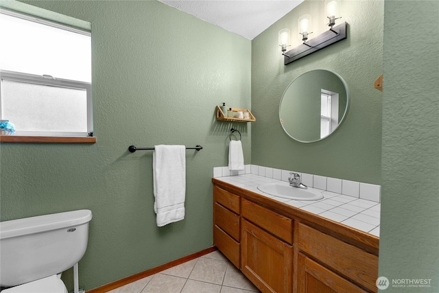 half bathroom featuring toilet, tile patterned flooring, baseboards, vanity, and a textured wall