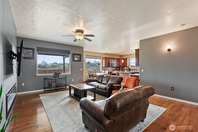 living room with wood finished floors, a ceiling fan, baseboards, and a textured ceiling