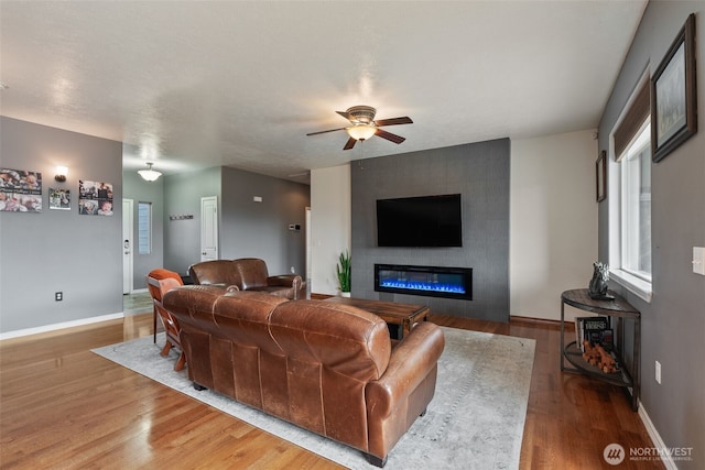 living room with ceiling fan, baseboards, wood finished floors, and a fireplace