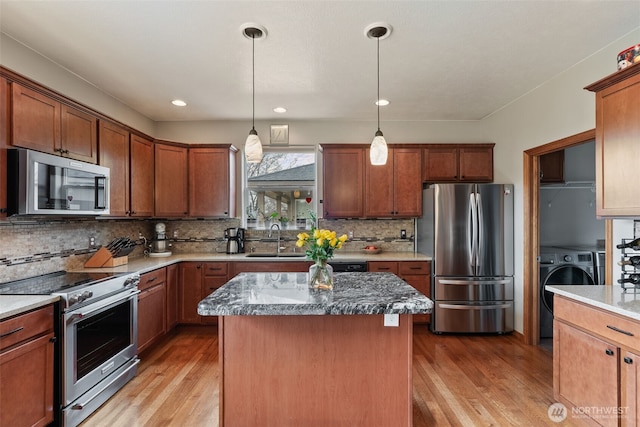 kitchen with appliances with stainless steel finishes, washer / clothes dryer, light wood-style floors, and a sink