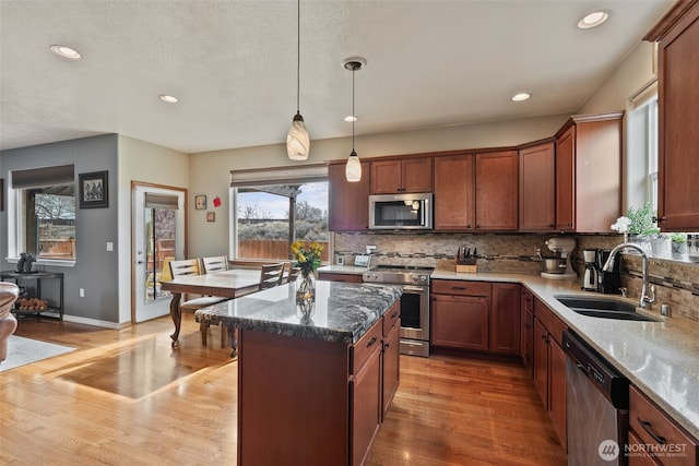 kitchen with light wood finished floors, a kitchen island, a sink, decorative backsplash, and appliances with stainless steel finishes