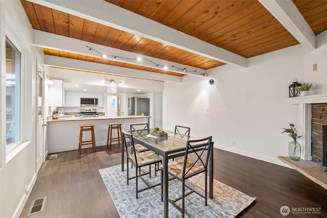 dining room with dark wood finished floors, visible vents, a fireplace with raised hearth, and baseboards