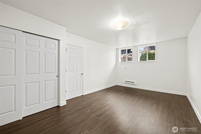 unfurnished bedroom featuring a closet, baseboards, dark wood-style flooring, and baseboard heating