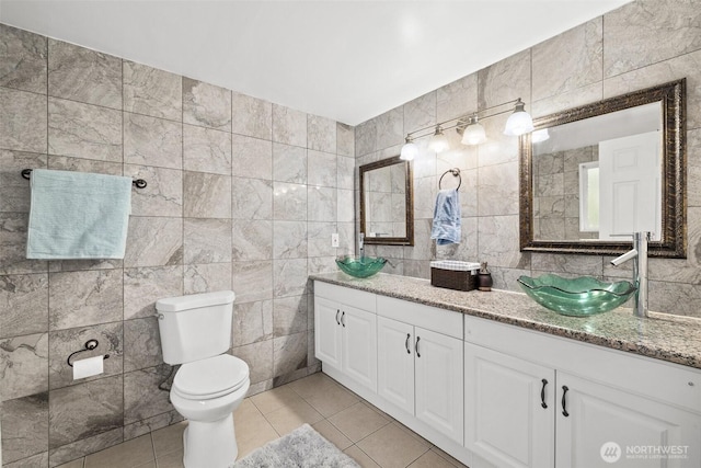 full bath featuring toilet, double vanity, tile patterned floors, tile walls, and a sink