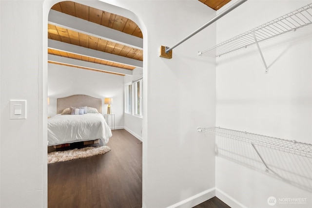 bedroom featuring beamed ceiling, wood finished floors, arched walkways, wooden ceiling, and baseboards