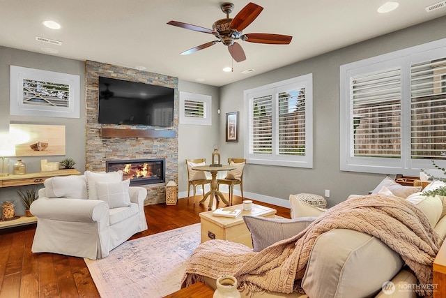 living room with visible vents, baseboards, a fireplace, wood finished floors, and a ceiling fan