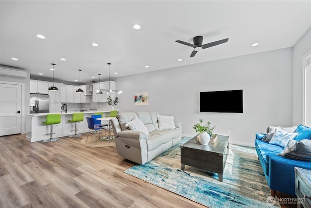 living area with baseboards, ceiling fan, light wood-type flooring, a wall unit AC, and recessed lighting