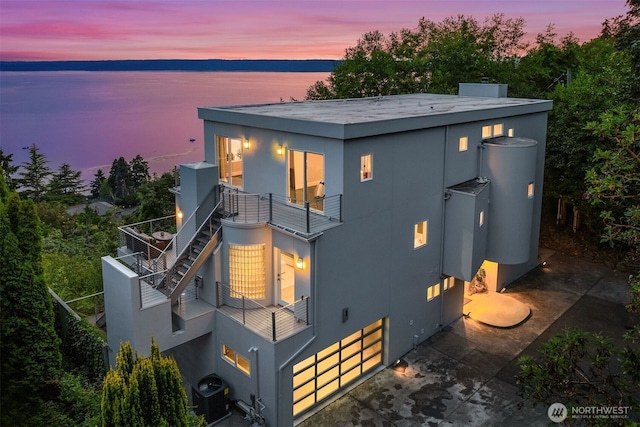 back of house with a balcony, central AC unit, a water view, and stucco siding