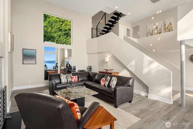 living area with stairs, wood finished floors, baseboards, and a towering ceiling