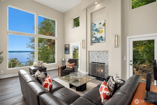 living room with baseboards, a water view, a fireplace, a high ceiling, and wood finished floors