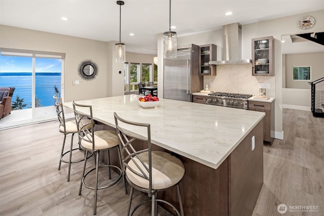 kitchen with a kitchen island, a breakfast bar, stove, wall chimney exhaust hood, and tasteful backsplash