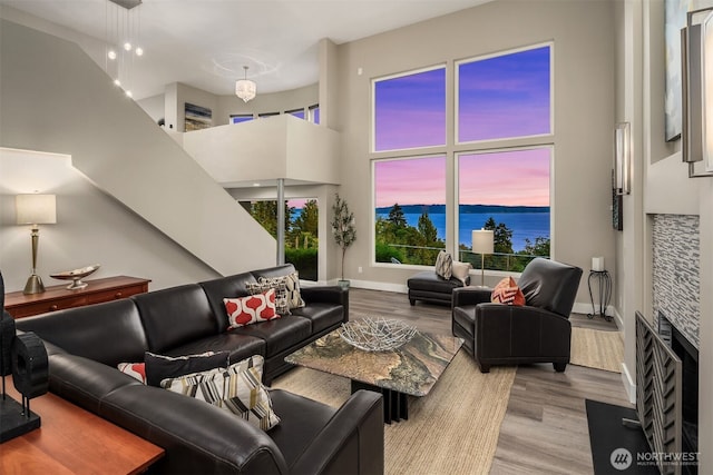 living area featuring wood finished floors, a water view, a towering ceiling, and baseboards