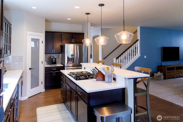 kitchen with a kitchen island, stainless steel fridge with ice dispenser, light countertops, a kitchen breakfast bar, and gas cooktop