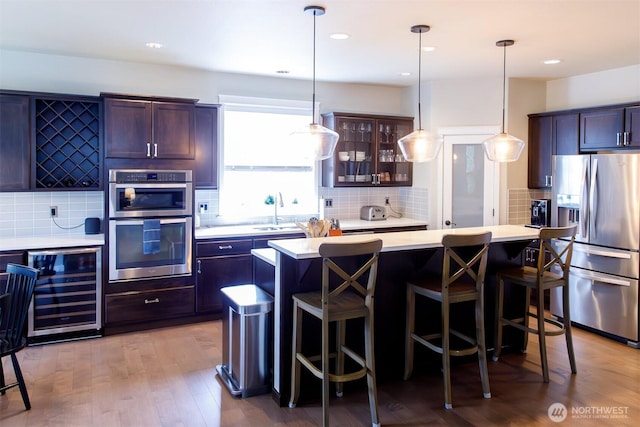 kitchen featuring a kitchen bar, a sink, stainless steel appliances, wine cooler, and light countertops