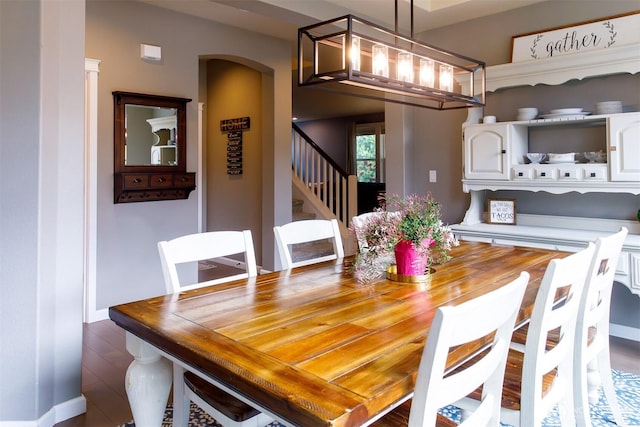 dining area featuring arched walkways, stairway, dark wood-type flooring, and baseboards