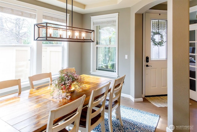 dining space featuring arched walkways, baseboards, and wood finished floors