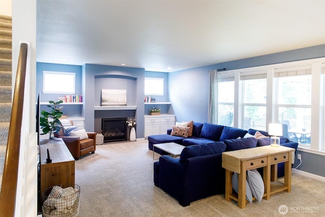 living room featuring stairs, a fireplace with flush hearth, light colored carpet, and a healthy amount of sunlight