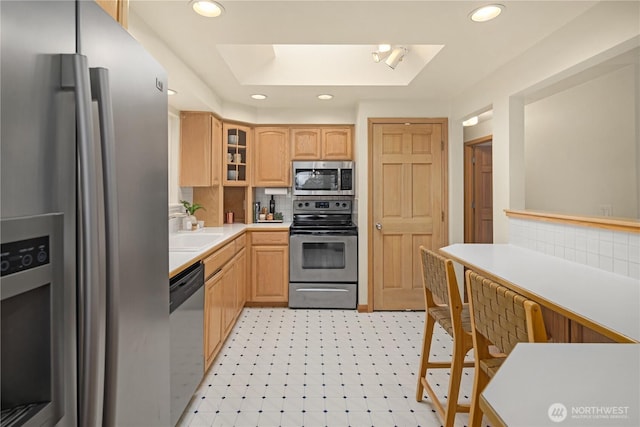 kitchen featuring light brown cabinets, glass insert cabinets, light countertops, a tray ceiling, and appliances with stainless steel finishes