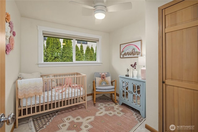 bedroom featuring a crib, baseboards, and a ceiling fan