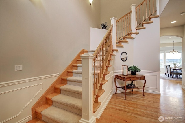 stairway with arched walkways, a wainscoted wall, a decorative wall, and wood finished floors